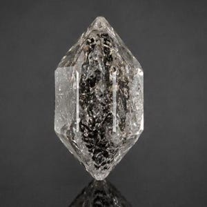 May include: A double-terminated clear quartz crystal featuring a hexagonal prism shape with sharp, pointed ends. The interior of the crystal contains dense, dark, needle-like inclusions that create a textured, black and gray internal pattern.