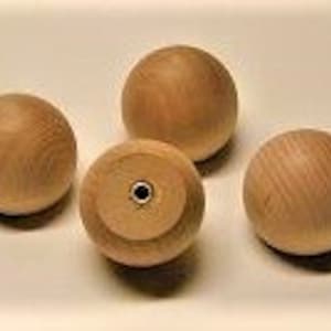 May include: Four unfinished wooden ball knobs. Three are smooth spheres, while one has a flat base with a metal insert. The natural wood grain is visible on each ball. These knobs are likely for furniture or craft projects.