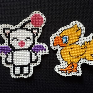 May include: Two cross-stitch embroidered patches featuring characters from the Final Fantasy video game series. The first patch is a white character with purple wings and a pink head. The second patch is a yellow bird-like character with orange feet and blue eyes.