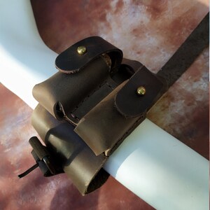 K&ouml;nnte beinhalten: Ein braunes Lederarmband mit zwei Taschen zum Tragen von Kleinigkeiten, gesichert mit Messing-Druckkn&ouml;pfen.