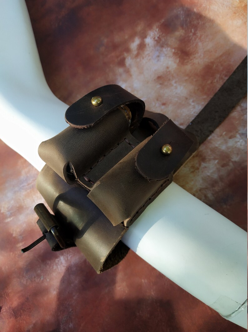 K&ouml;nnte beinhalten: Ein braunes Lederarmband mit zwei Taschen zum Tragen von Kleinigkeiten, gesichert mit Messing-Druckkn&ouml;pfen.