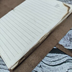 May include: A brown leather bound journal with a white lined paper interior. The journal has a burnt edge and the words "Date, Month, Place" are written on the last page.