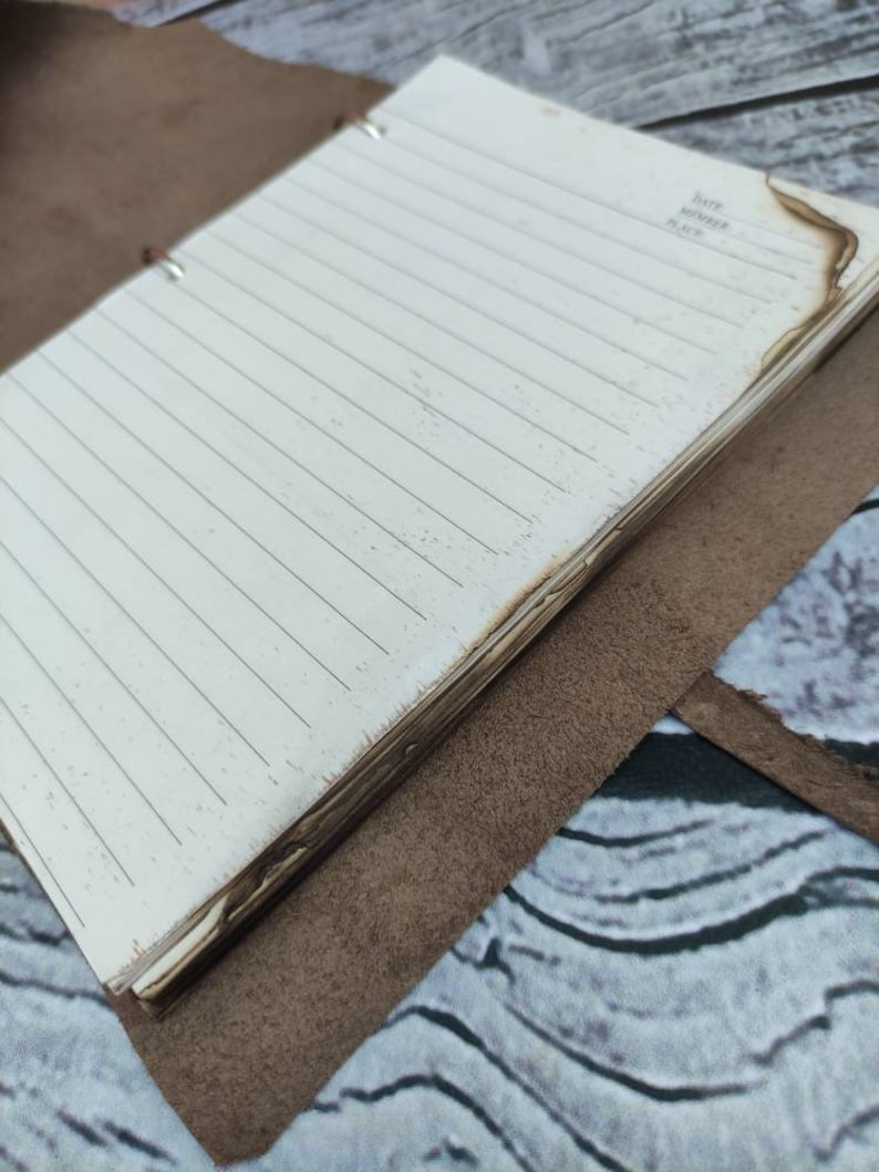 May include: A brown leather bound journal with a white lined paper interior. The journal has a burnt edge and the words "Date, Month, Place" are written on the last page.