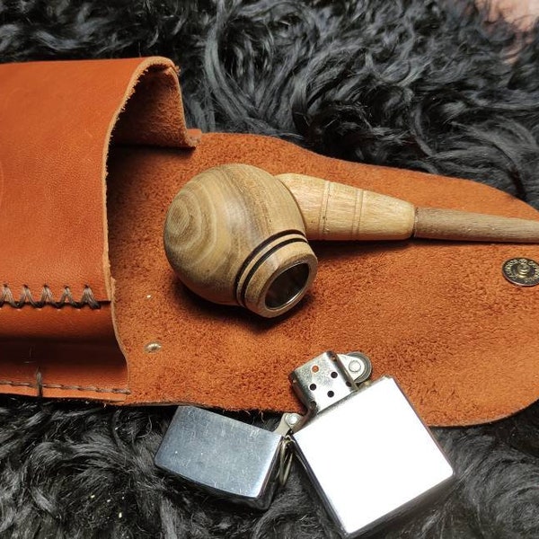 May include: A wooden pipe with a brown leather carrying case and a silver lighter. The pipe is made of light brown wood with dark brown accents. The case is made of brown leather with a stitched edge. The lighter is made of silver metal and has a black plastic top.