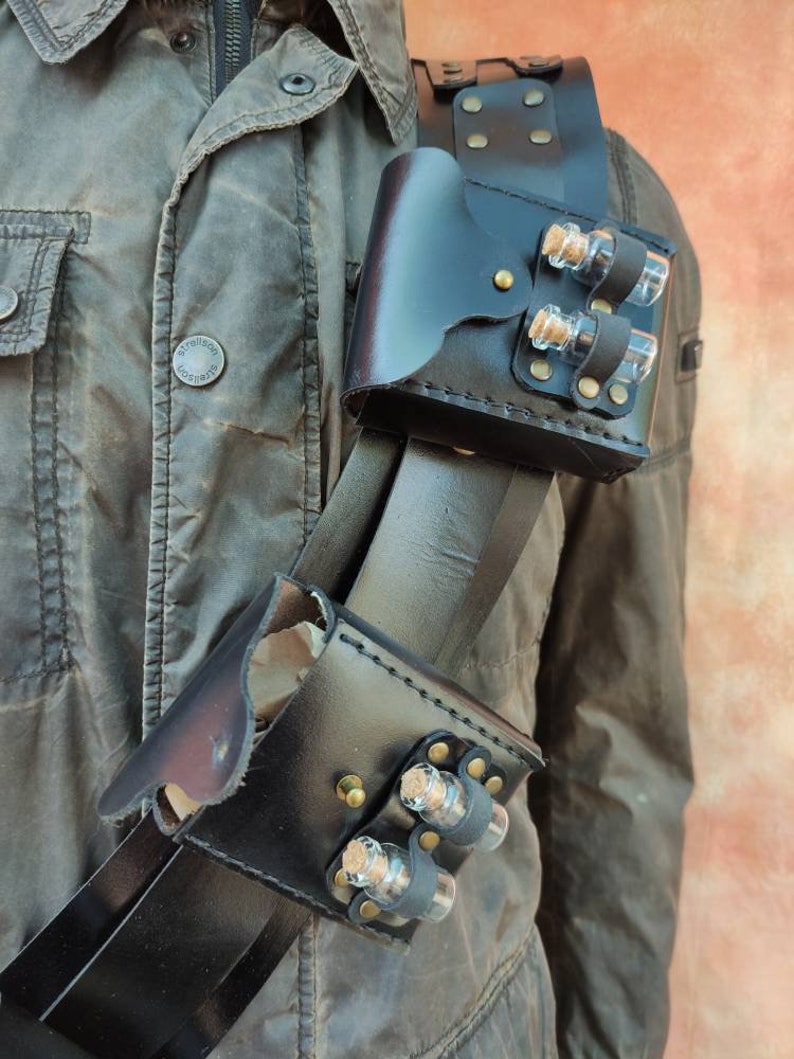 May include: A black leather shoulder holster with two pouches, each holding three small glass vials with cork stoppers. The holster is worn over a brown jacket.