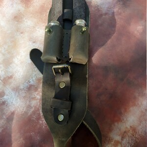 K&ouml;nnte beinhalten: Ein brauner Lederg&uuml;rtel mit zwei Taschen zum Tragen kleiner Gegenst&auml;nde. Die Taschen haben Metallschnallen und sind mit N&auml;hten am G&uuml;rtel befestigt. Der G&uuml;rtel hat eine Schnalle und eine Schlaufe zum Befestigen an einer G&uuml;rtelschlaufe.