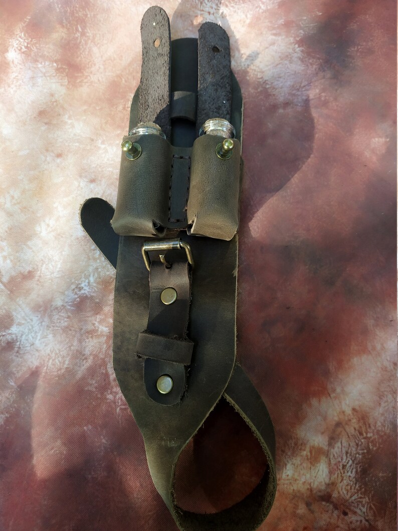 K&ouml;nnte beinhalten: Ein brauner Lederg&uuml;rtel mit zwei Taschen zum Tragen kleiner Gegenst&auml;nde. Die Taschen haben Metallschnallen und sind mit N&auml;hten am G&uuml;rtel befestigt. Der G&uuml;rtel hat eine Schnalle und eine Schlaufe zum Befestigen an einer G&uuml;rtelschlaufe.