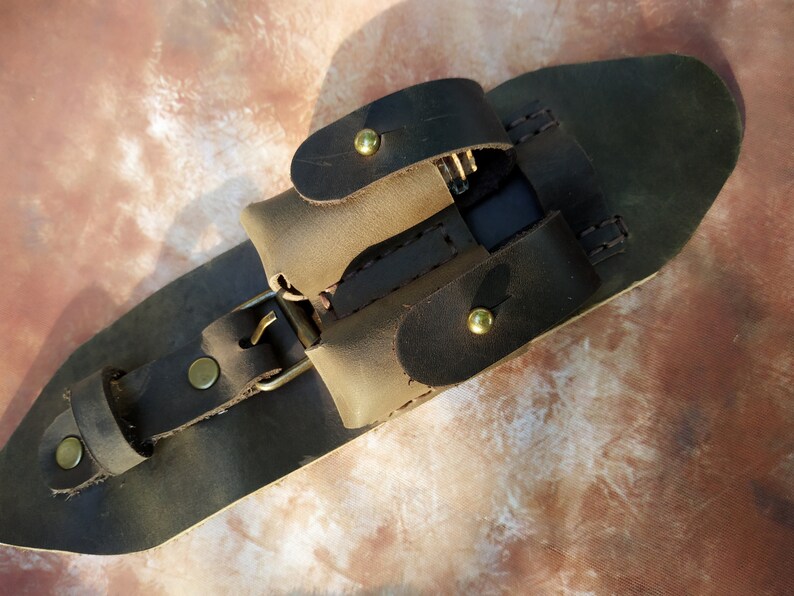 K&ouml;nnte beinhalten: Ein brauner Lederg&uuml;rtel mit einer Schnalle und einer kleinen Tasche. Die Tasche hat eine Klappe, die mit einem Druckknopf geschlossen wird. Der G&uuml;rtel ist so konzipiert, dass er einen kleinen Gegenstand wie ein Telefon oder eine Brieftasche aufnehmen kann.