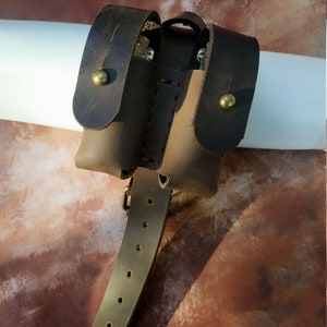 K&ouml;nnte beinhalten: Ein braunes Lederbeutel mit zwei F&auml;chern und einer G&uuml;rtelschlaufe. Der Beutel hat zwei Messing-Druckkn&ouml;pfe und ist f&uuml;r die Aufbewahrung von kleinen Gegenst&auml;nden konzipiert.
