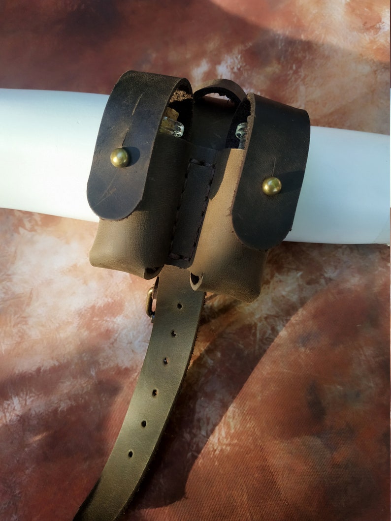 K&ouml;nnte beinhalten: Ein braunes Lederbeutel mit zwei F&auml;chern und einer G&uuml;rtelschlaufe. Der Beutel hat zwei Messing-Druckkn&ouml;pfe und ist f&uuml;r die Aufbewahrung von kleinen Gegenst&auml;nden konzipiert.