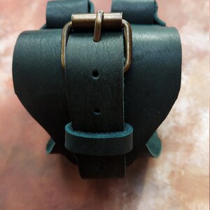 K&ouml;nnte beinhalten: Ein dunkelgr&uuml;nes Lederarmband mit einer Messing-Schnalle. Das Armband ist verstellbar und hat ein schlichtes Design.