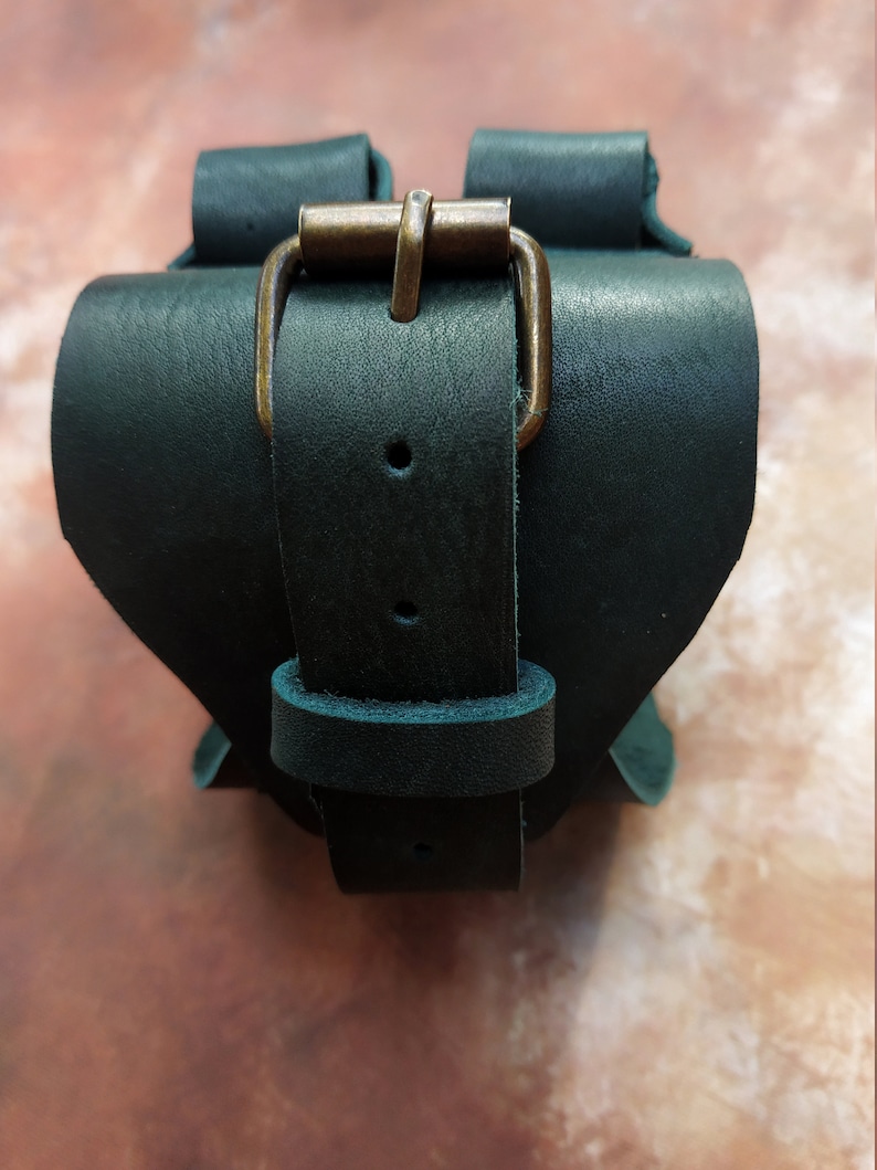 K&ouml;nnte beinhalten: Ein dunkelgr&uuml;nes Lederarmband mit einer Messing-Schnalle. Das Armband ist verstellbar und hat ein schlichtes Design.