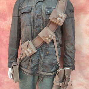 May include: A brown leather belt with multiple pouches and straps. The belt has a buckle and is worn over a brown jacket.