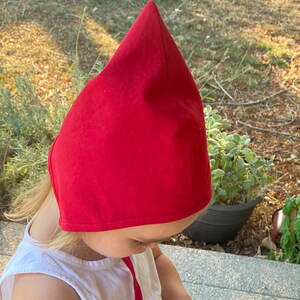 May include: A bright red, pointed hat, likely for a child, is the focal point of the image. The hat is made of a solid, opaque material. The hat is worn by a person wearing a white shirt.