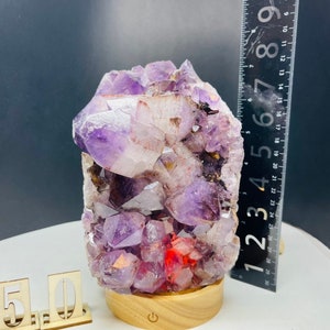 May include: A purple amethyst crystal cluster with red inclusions, mounted on a wooden base with a light switch. The crystal is approximately 7 inches tall.