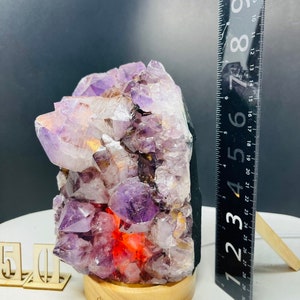 May include: A purple amethyst crystal lamp with a wooden base. The crystal is lit from within, creating a warm glow. The lamp is approximately 6 inches tall.