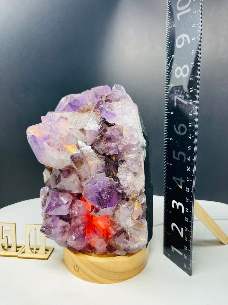 May include: A purple amethyst crystal lamp with a wooden base. The crystal is lit from within, creating a warm glow. The lamp is approximately 6 inches tall.