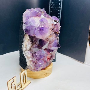 May include: A large amethyst crystal cluster on a wooden base with a light switch. The crystal is purple and has a natural, rough texture. The base is made of wood and has a natural finish.