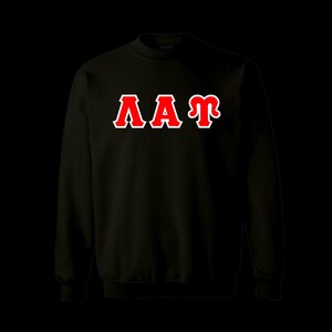May include: A black long-sleeve crewneck sweatshirt featuring the Greek letters Lambda, Alpha, and Tau in red with a white outline centered on the chest. The garment has a ribbed collar, cuffs, and hem, providing a standard fit and solid color.
