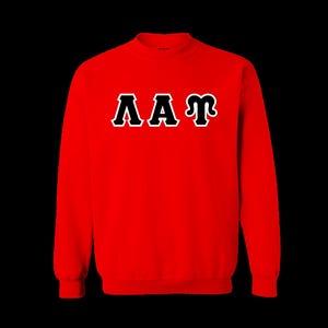 May include: A bright red long-sleeve crewneck sweatshirt featuring the Greek letters Lambda, Alpha, and Phi printed across the chest in black with a white outline. The garment has a ribbed collar, cuffs, and hem, providing a clean finish.