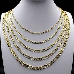 May include: A set of six gold chain necklaces of varying widths, all featuring a classic figaro link design. The chains are layered on a white mannequin bust, showcasing their different lengths and thicknesses.