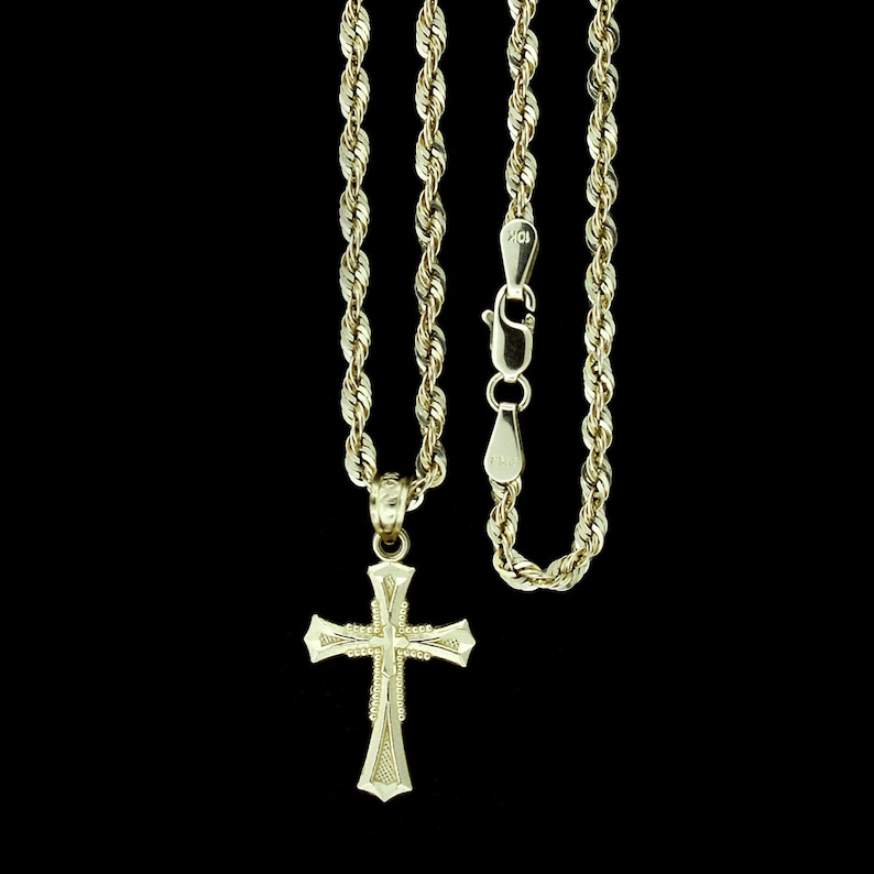 May include: A gold rope chain necklace with a gold cross pendant. The cross has a detailed design and is hanging from a delicate chain.