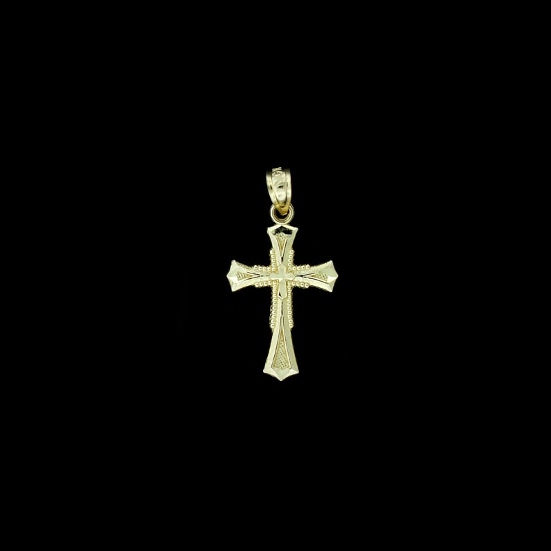 May include: A gold cross pendant with a detailed design. The cross has a textured surface and a small loop at the top for attaching a chain.