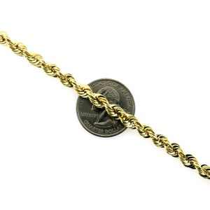 May include: A gold rope chain necklace next to a US quarter dollar coin. The chain is thick and has a shiny finish.