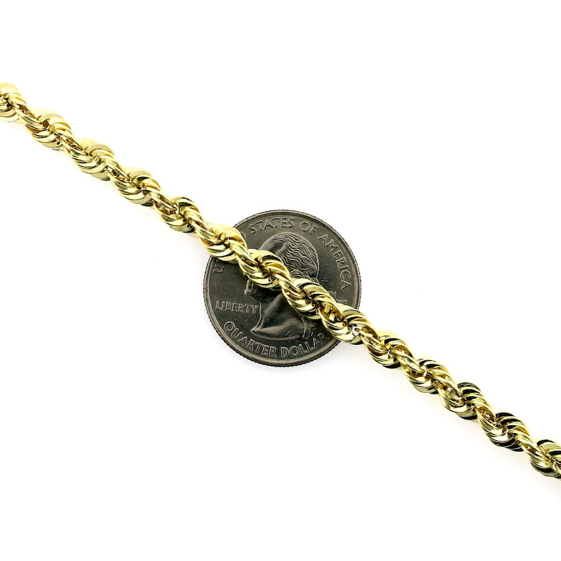May include: A gold rope chain necklace next to a US quarter dollar coin. The chain is thick and has a shiny finish.