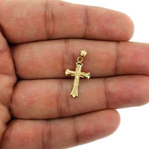 May include: A gold-toned cross pendant with a detailed design. The pendant is small and delicate, with a simple, elegant style.