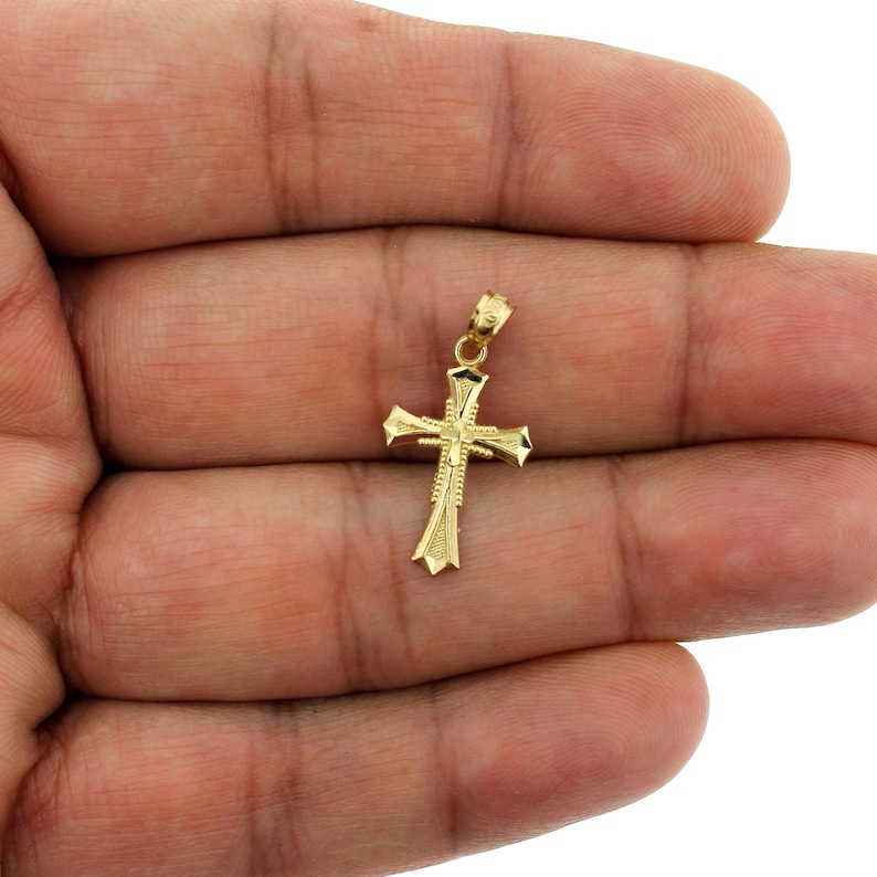 May include: A gold-toned cross pendant with a detailed design. The pendant is small and delicate, with a simple, elegant style.