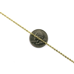 May include: A gold rope chain necklace, shown next to a US quarter for size comparison. The chain is made of a braided, twisted design.