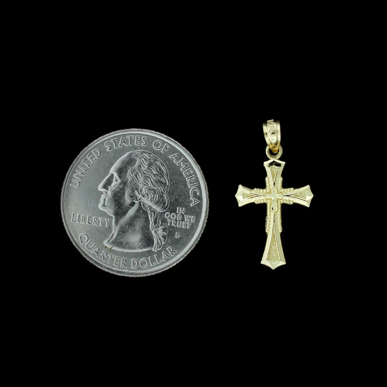 May include: A gold-colored cross pendant, shown next to a US quarter for size comparison. The cross has a simple design with a slightly rounded edge.