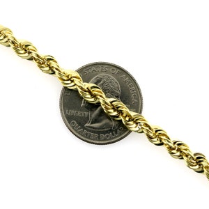 May include: A gold rope chain necklace next to a US quarter dollar coin. The chain is thick and has a shiny finish.