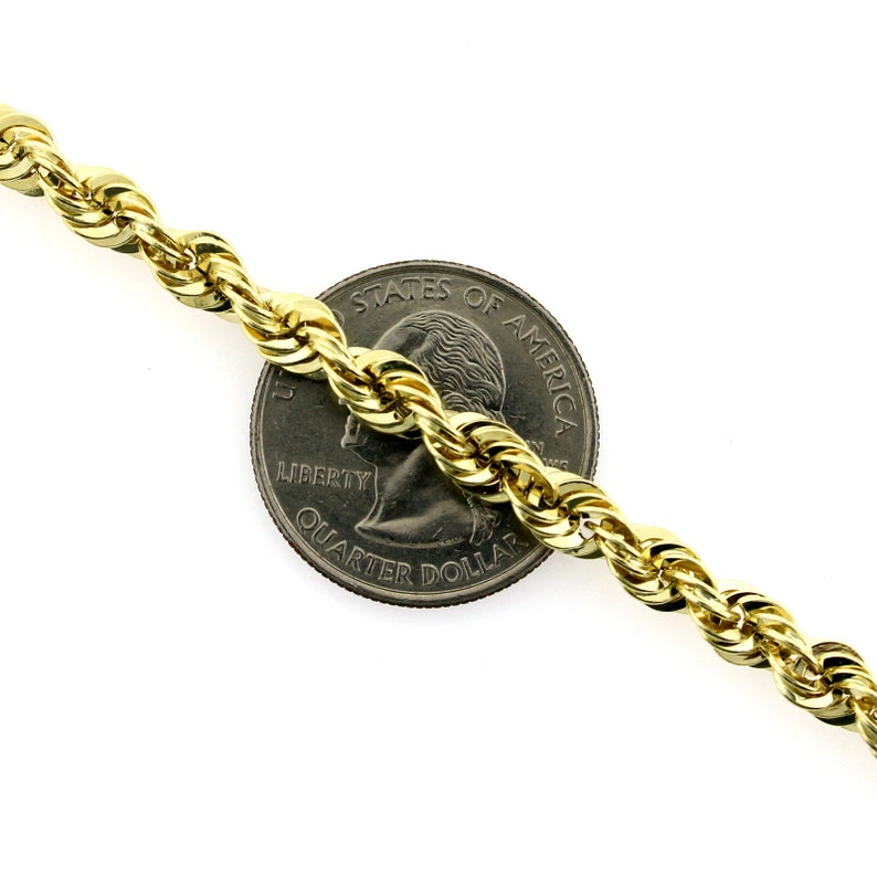 May include: A gold rope chain necklace next to a US quarter dollar coin. The chain is thick and has a shiny finish.