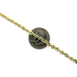 May include: A gold rope chain necklace, laying on a white surface, with a US quarter dollar coin for size comparison.