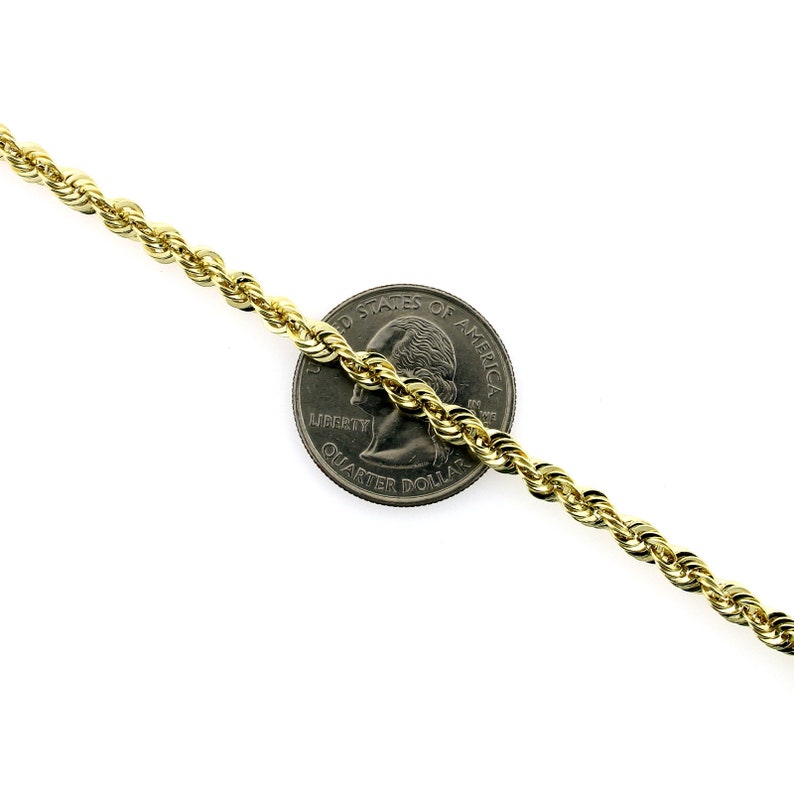 May include: A gold rope chain necklace, laying on a white surface, with a US quarter dollar coin for size comparison.