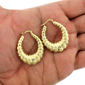 May include: A pair of gold hoop earrings with a textured, ridged design. The earrings are oval shaped and have a polished finish.