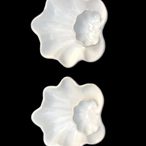 May include: Two white ceramic serving dishes with a flower-like design. Each dish has a large, wavy-edged outer bowl and a smaller, central bowl. The dishes are glossy and appear to be new.