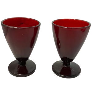 May include: Two ruby red, cone-shaped glasses with a rounded base. The glasses have a smooth, glossy finish and are likely made of glass. The design is simple and elegant, suitable for serving beverages.