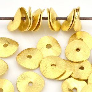 May include: A group of 17 gold-colored metal beads with a textured surface and a hole in the center. The beads are arranged in a pile on a white surface.