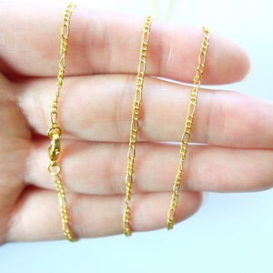 May include: A gold chain necklace with a lobster clasp closure. The chain is a delicate, fine, and flat curb style.