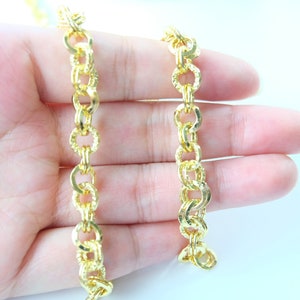 May include: A gold chain necklace with a textured, linked design. The chain is shown on a hand, with two strands of the chain.