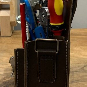 May include: A brown leather tool bag with a metal buckle and a strap. The bag is filled with tools, including a red and yellow screwdriver, a blue wire stripper, and a silver tool. The bag is labeled "V2 70mm".