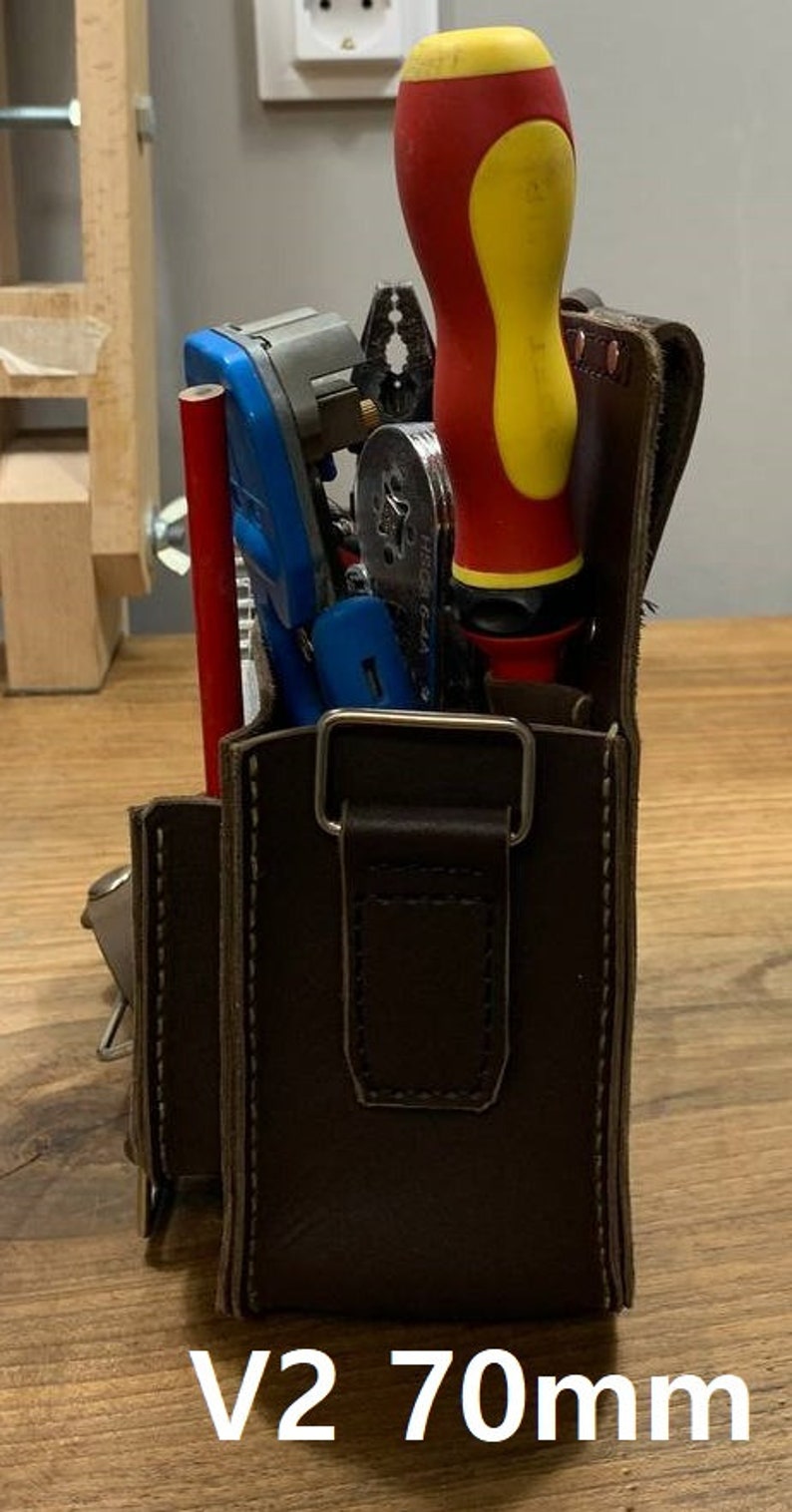 May include: A brown leather tool bag with a metal buckle and a strap. The bag is filled with tools, including a red and yellow screwdriver, a blue wire stripper, and a silver tool. The bag is labeled "V2 70mm".