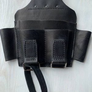 Peut inclure: Ceinture &agrave; outils en cuir noir avec plusieurs poches et une poign&eacute;e en boucle. La ceinture est dot&eacute;e d'une fermeture &agrave; boucle et est con&ccedil;ue pour &ecirc;tre port&eacute;e autour de la taille.