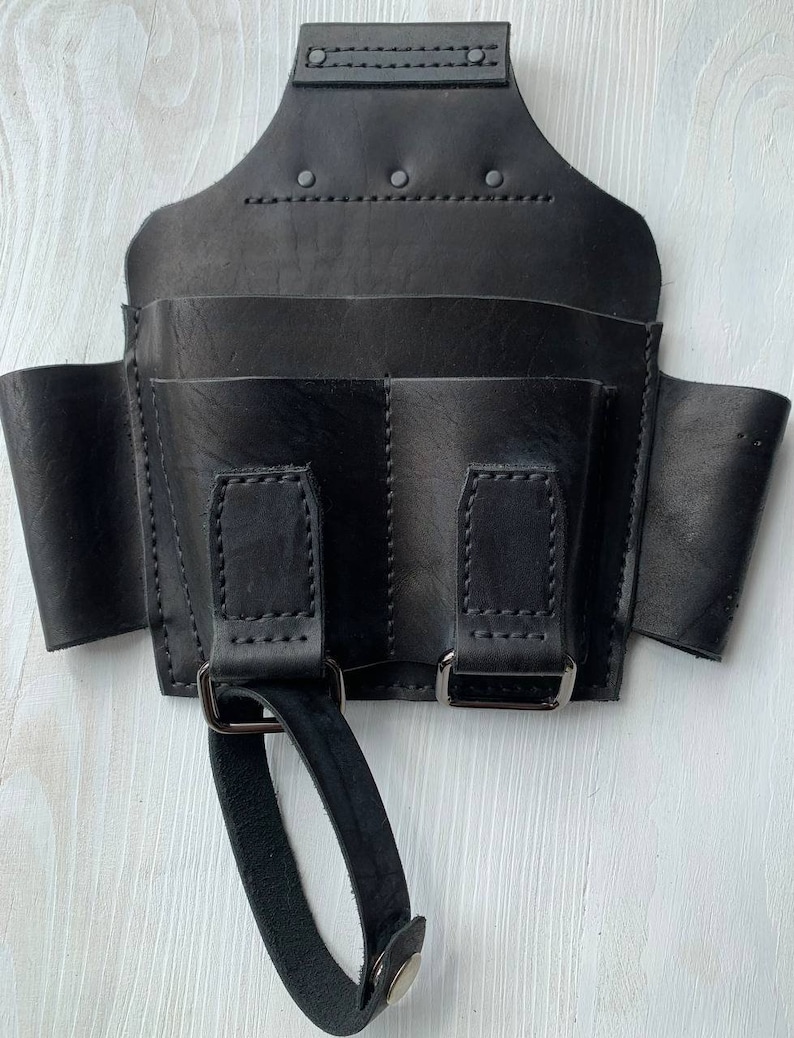 Peut inclure: Ceinture &agrave; outils en cuir noir avec plusieurs poches et une poign&eacute;e en boucle. La ceinture est dot&eacute;e d'une fermeture &agrave; boucle et est con&ccedil;ue pour &ecirc;tre port&eacute;e autour de la taille.
