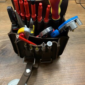 May include: A brown leather tool belt with a variety of tools, including screwdrivers, pliers, and a pencil. The belt has a loop for attaching to a belt.