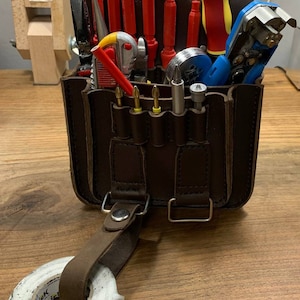 May include: A brown leather tool bag with a variety of tools, including screwdrivers, pliers, wire strippers, and electrical tape. The bag has a strap and a buckle.
