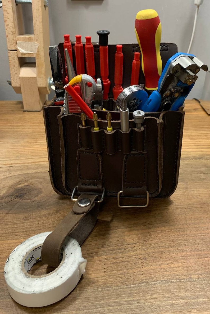 May include: A brown leather tool bag with a variety of tools, including screwdrivers, pliers, wire strippers, and electrical tape. The bag has a strap and a buckle.